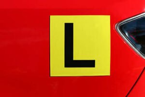 Yellow Australian L plate learner driver sign mounted on the back of a vehicle

Caption: Getting your L plates is step one in Australia.